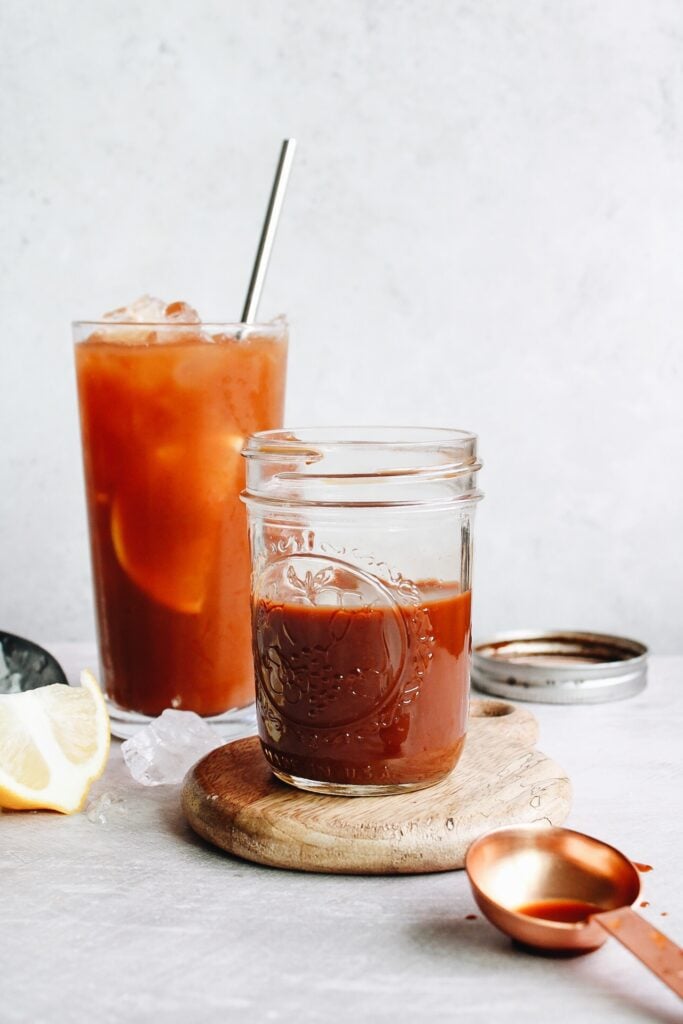 black tea concentrate in a small glass jar with a glass of iced tea behind it