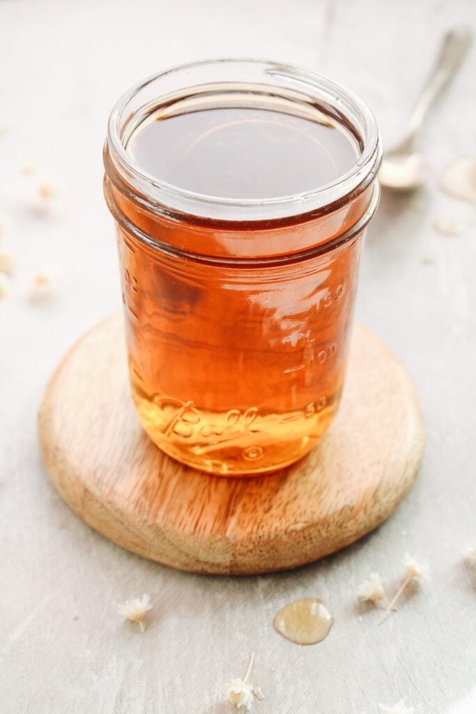 chamomile syrup in a glass jar on a wooden coaster