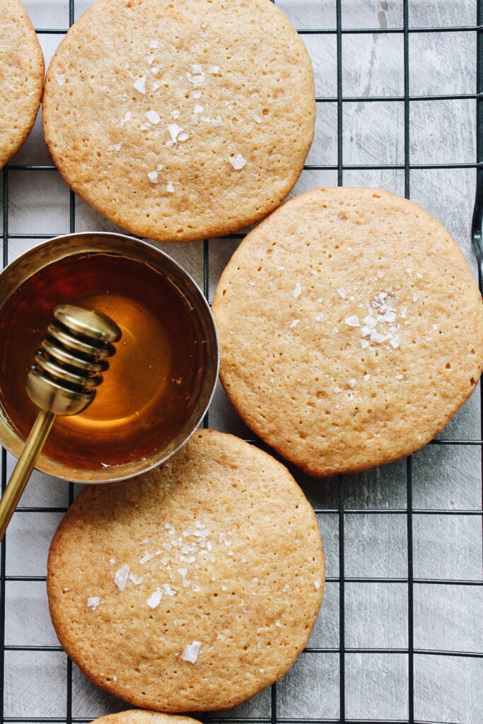 honey cookies with sea salt on a black wire cooling rack with a dish of honey