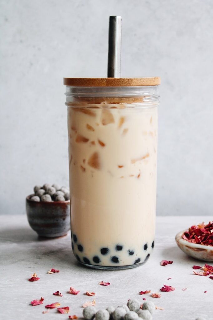 rose milk tea in a boba glass with rose petals and tapioca pearls scattered around