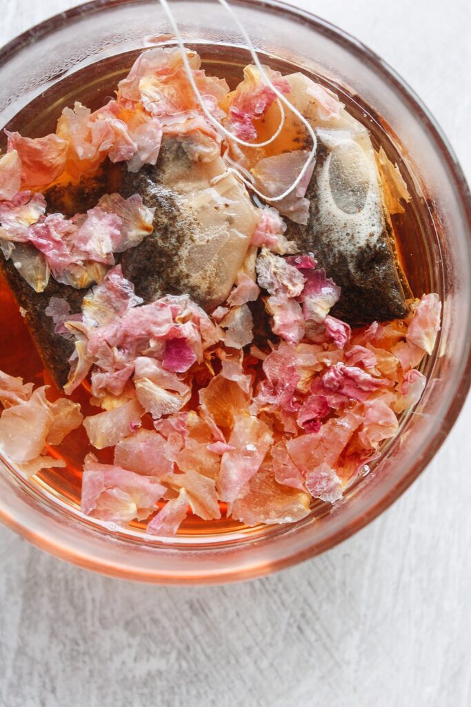 black tea brewing with rose petals in a clear glass mug