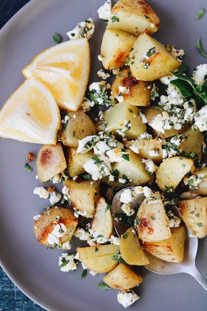 mediterranean potatoes on a gray plate with a serving spoon and lemon wedges