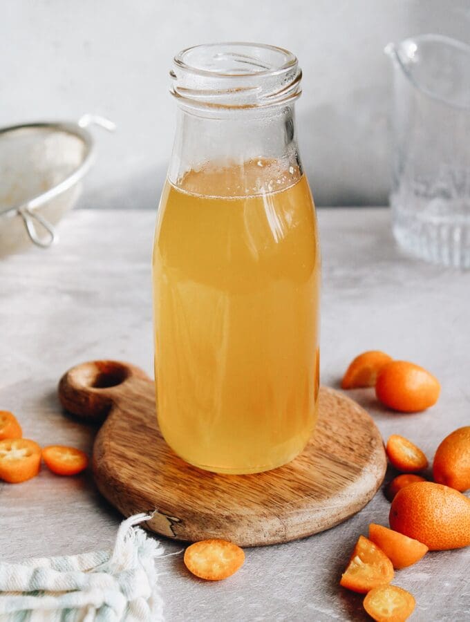 kumquat syrup in a glass jar on a wooden coaster
