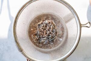 lavender flowers being strained out of milk through a mesh sieve