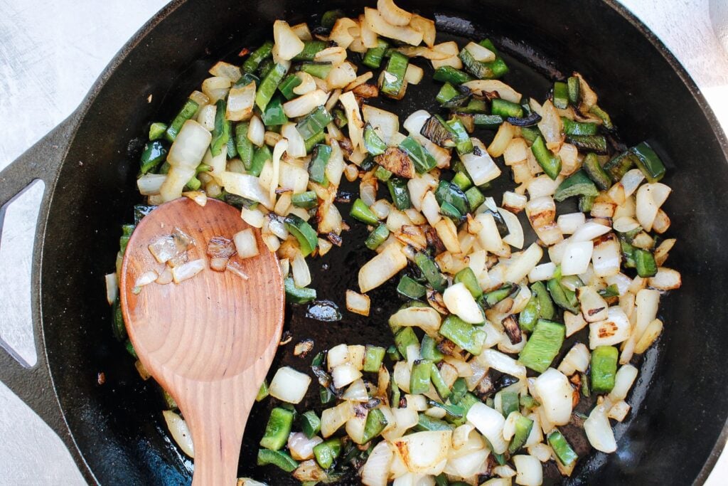 chopped pablano pepper and onion cooking in a cast iron skillet with butter