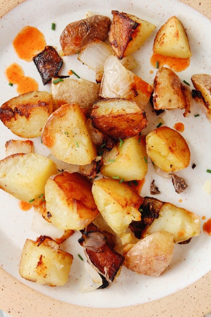 skillet fried breakfast potatoes on a plate with hot sauce and chives