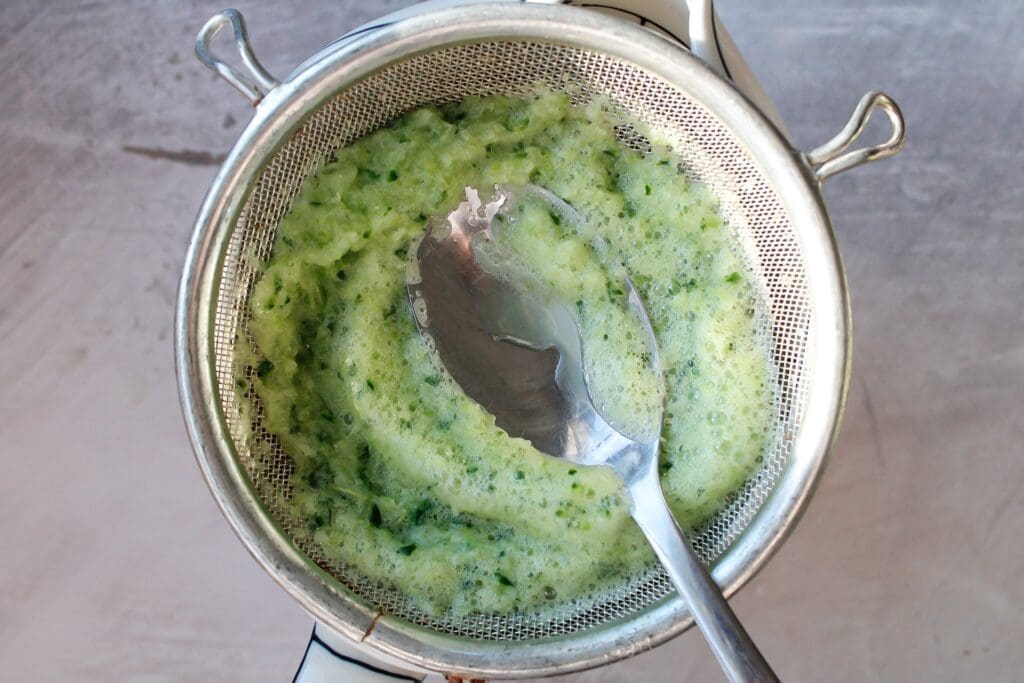cucumber celery juice being strained through a mesh sieve