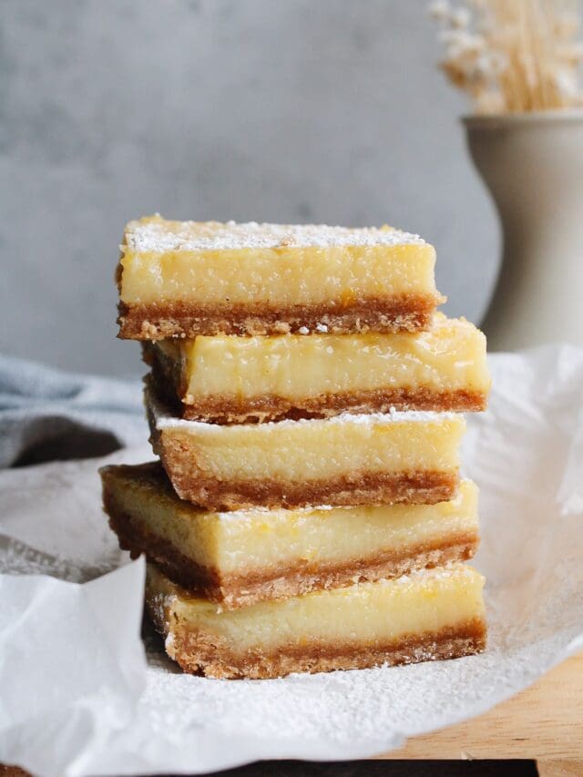 lemon squares with graham cracker crust stacked on a piece of parchment paper