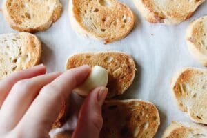 raw garlic clove being rubbed on a toasted slice of a baguette