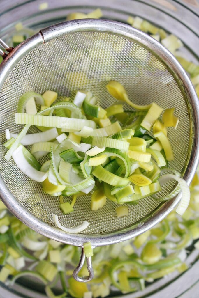 washed leeks being removed from bowl of water with a small strainer