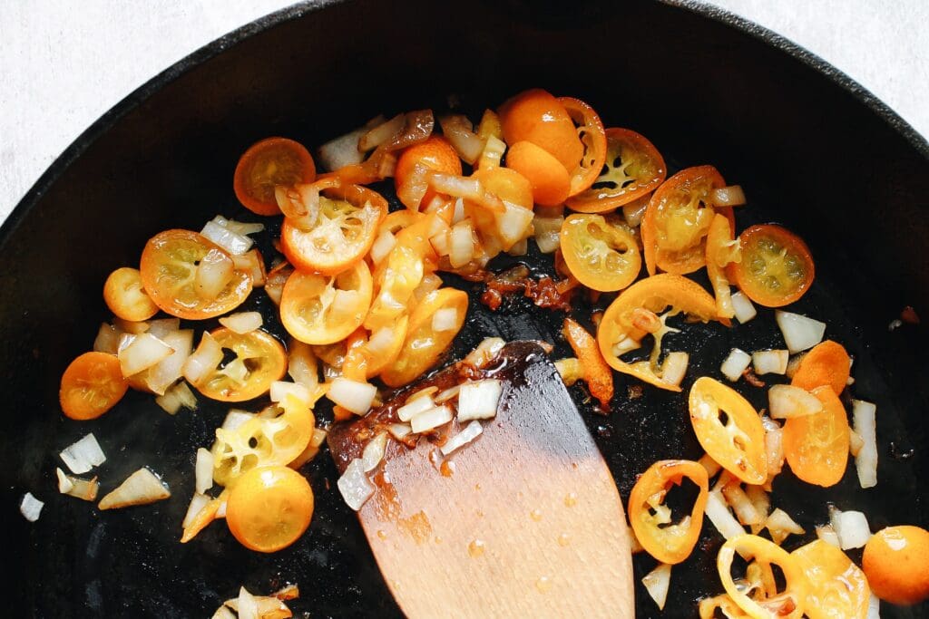 kumquats and onions cooking in a cast-iron skillet