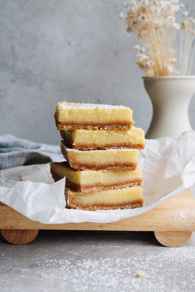 lemon squares with graham cracker crust stacked on a piece of parchment