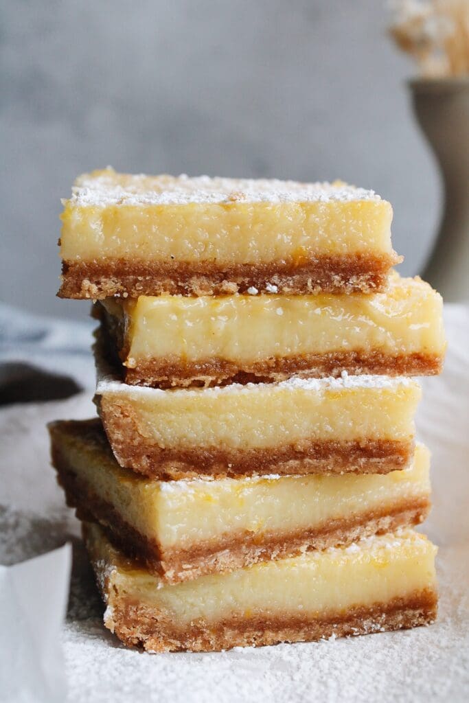close up of lemon squares stacked on a piece of parchment paper