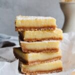 lemon squares with graham cracker crust stacked on a piece of parchment paper