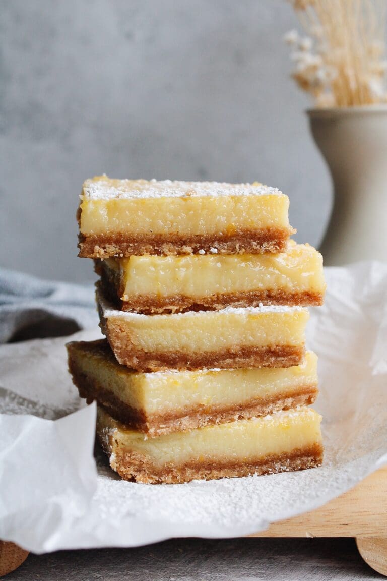 lemon squares with graham cracker crust stacked on a piece of parchment paper