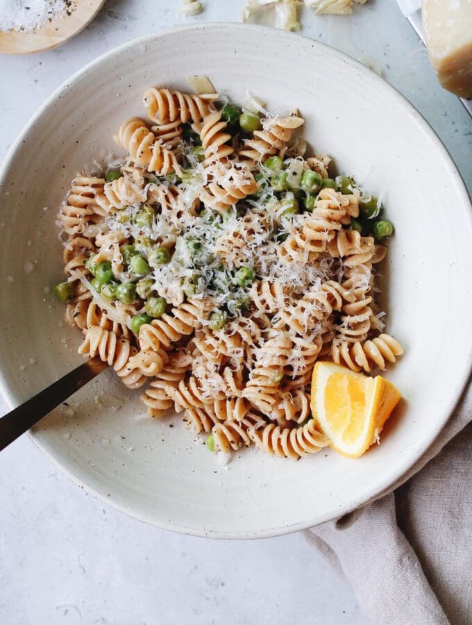 pasta with peas in a white bowl with a lemon wedge