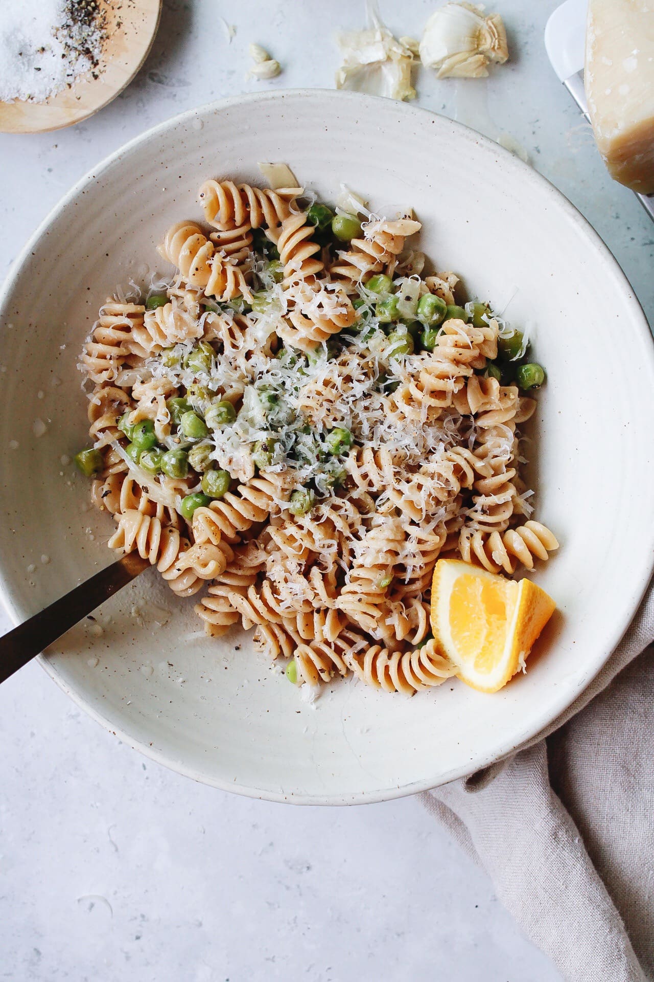pasta with peas in a white bowl topped with parmesan and a lemon wedge