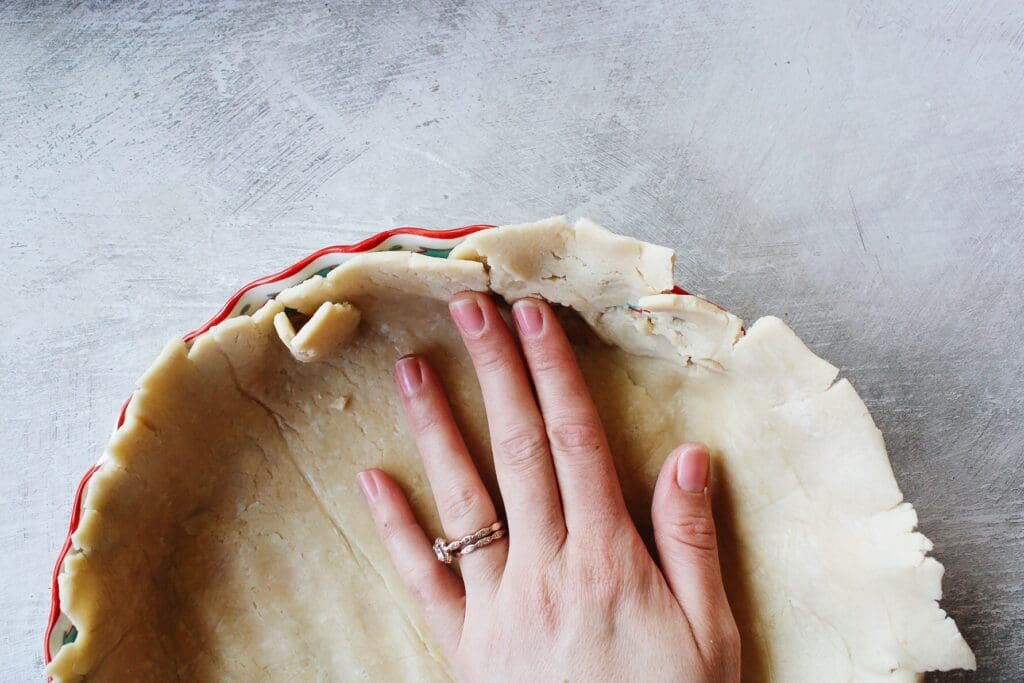quiche crust being pressed against the edge of a baking dish with hands