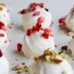 rose white chocolate truffles on a baking sheet topped with chopped pistachio, strawberries and rose petals.