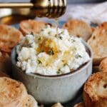 honey being drizzled over a bowl with whipped feta