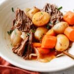 dutch oven pot roast in a white bowl with a golden fork