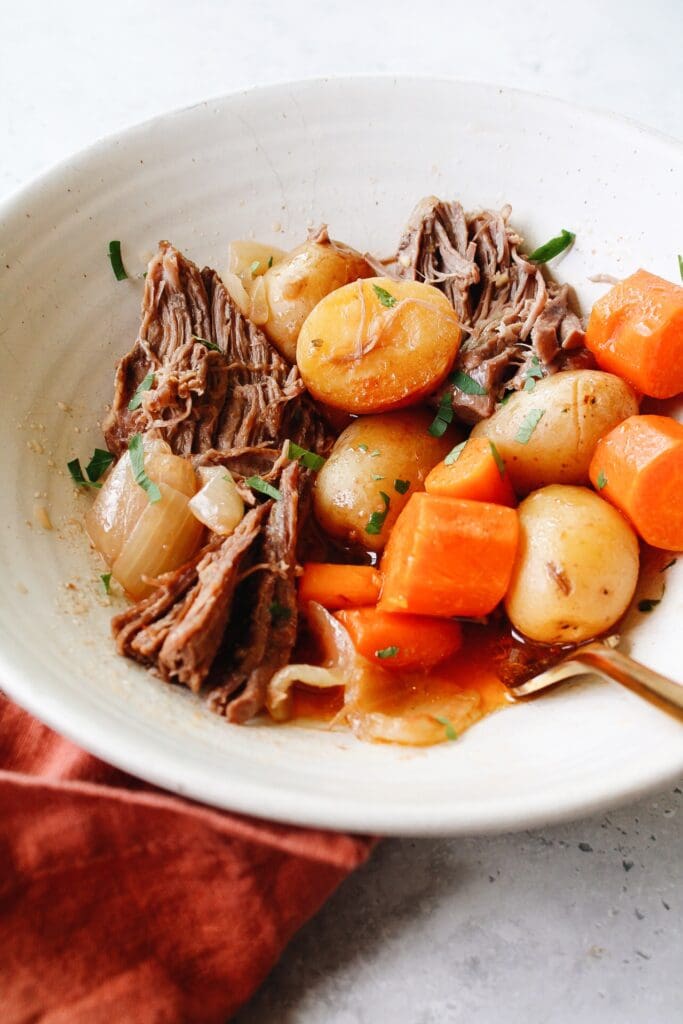 dutch oven pot roast in a white bowl with a golden fork 