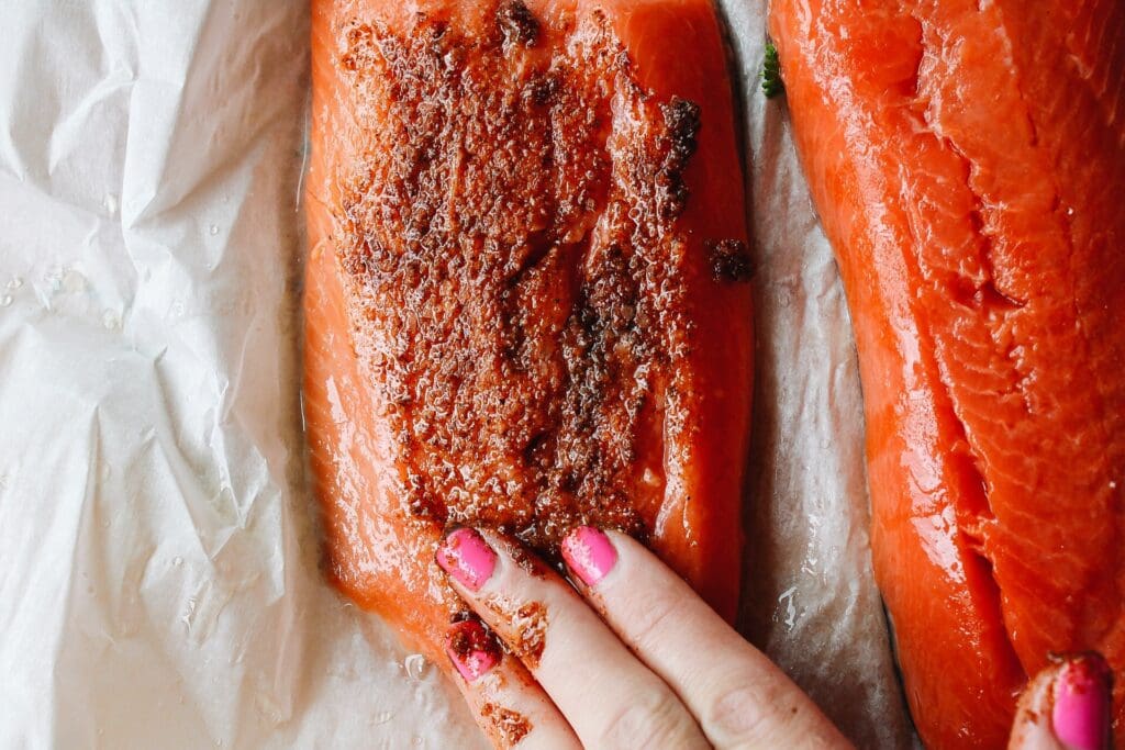spice rub being applied to salmon fillet