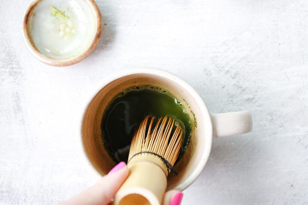 matcha powder and hot water being whisked in a mug with a matcha whisk