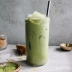 oat milk matcha latte in a clear glass with a metal straw
