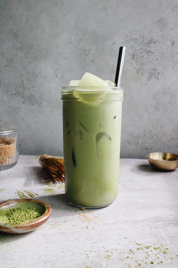 oat milk matcha latte in a clear glass with a metal straw
