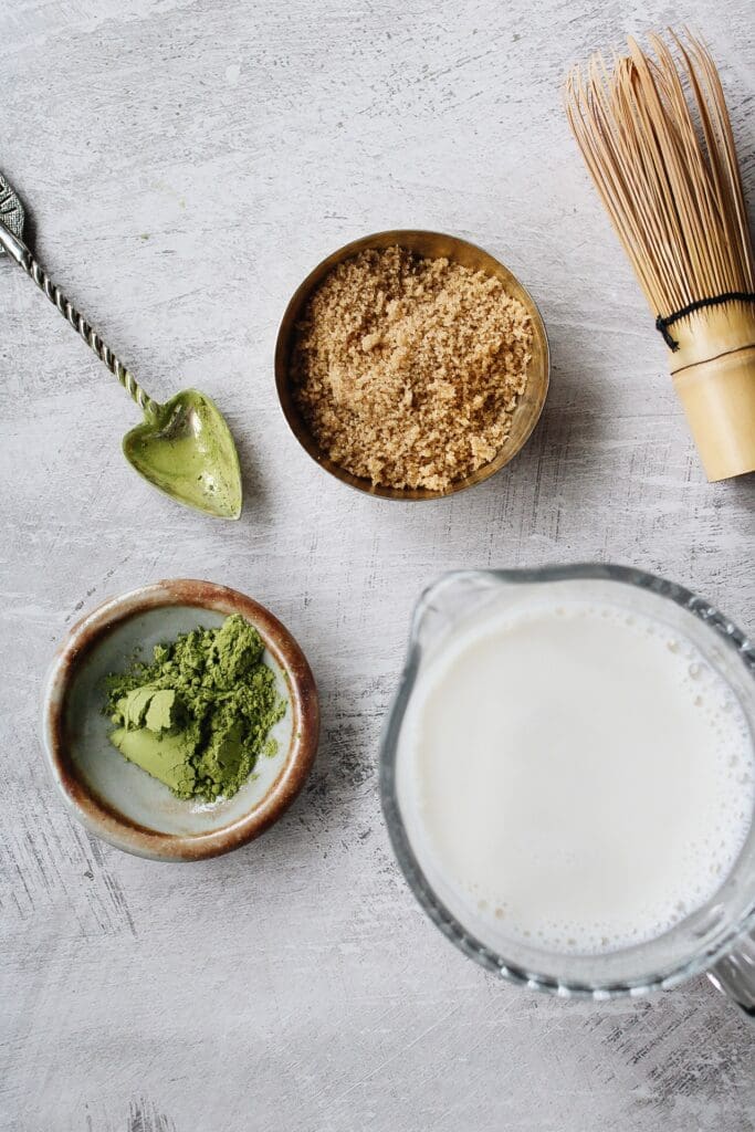 ingredients for an oat milk matcha latte on a gray background