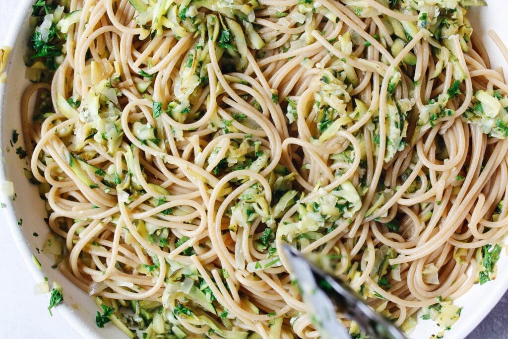 veggies and pasta in a nonstick skillet being stirred with tongs