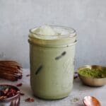 rose matcha latte in a glass jar with dried rose petals scattered around
