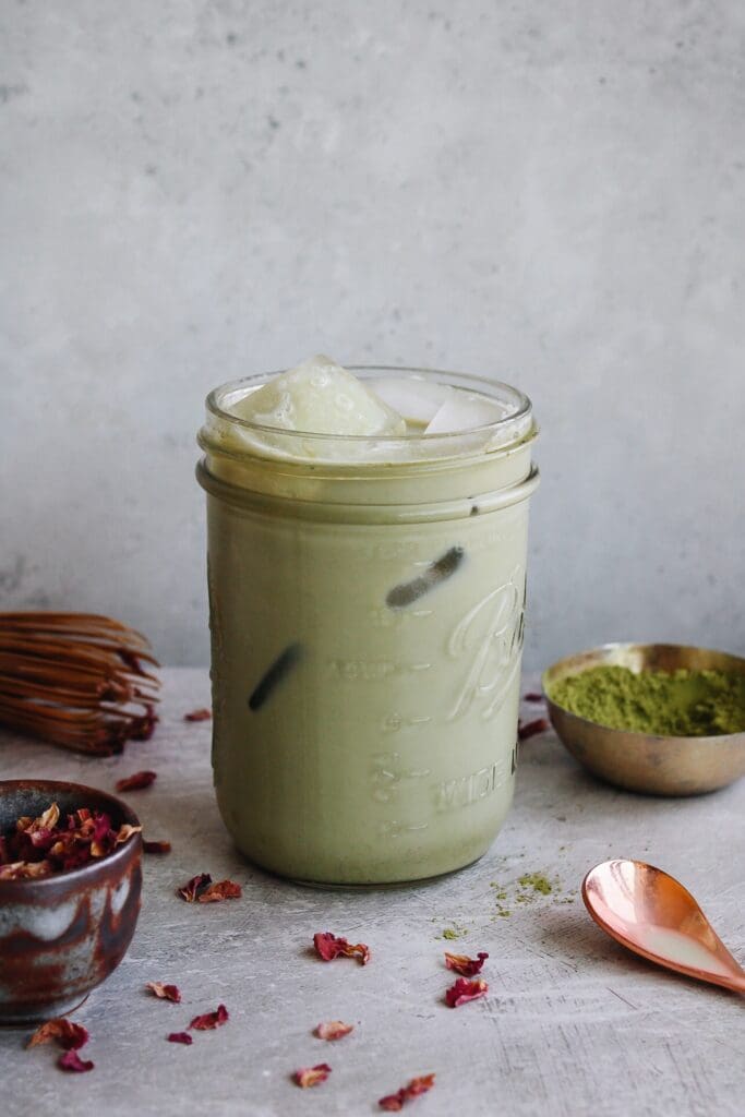 rose matcha latte in a glass jar with dried rose petals scattered around
