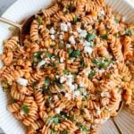 spicy pasta salad in a large white bowl with gold serving spoons
