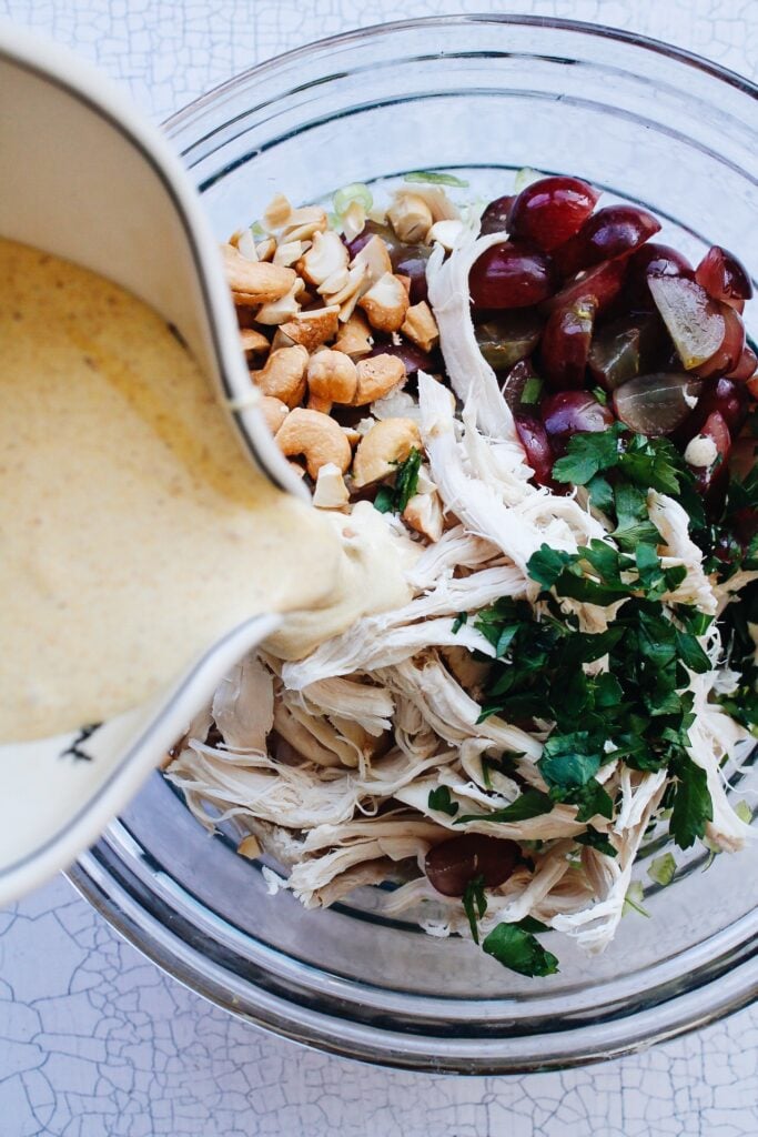 cream curry dressing being added to bowl with chicken salad ingredients