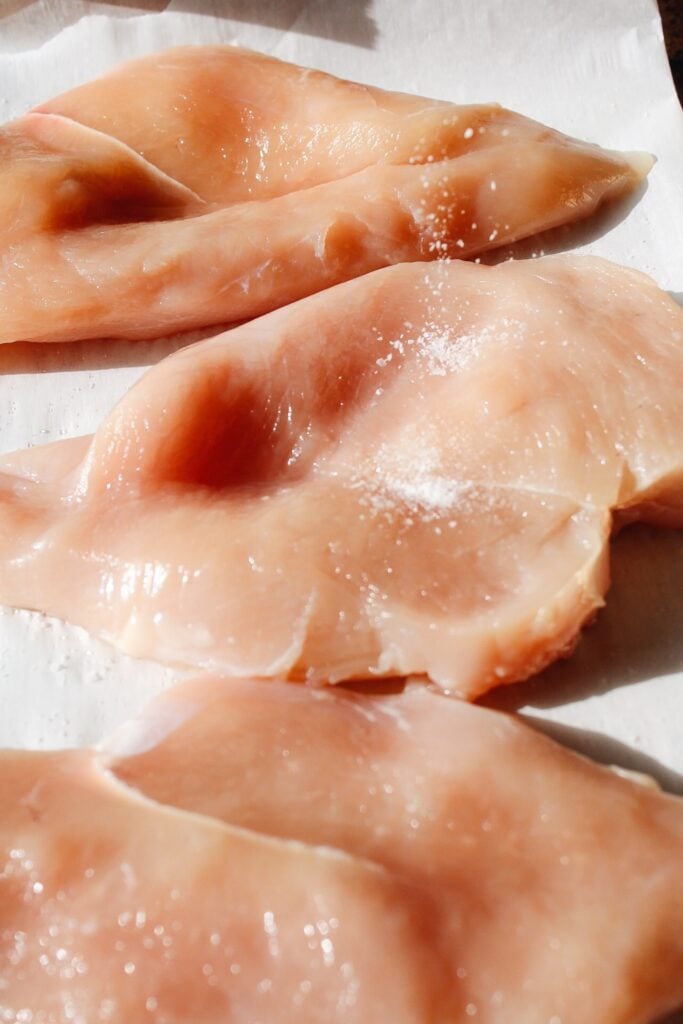 salt being sprinkled on top of a raw chicken breast