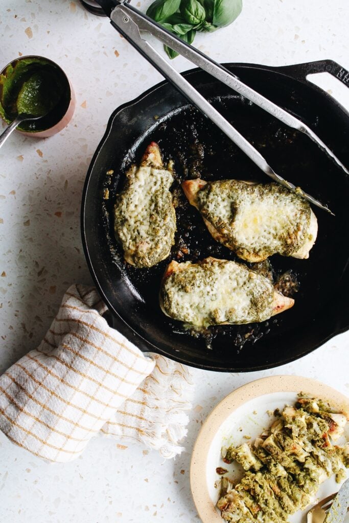 pesto baked chicken in cast iron skillet with pesto and basil outside the pan
