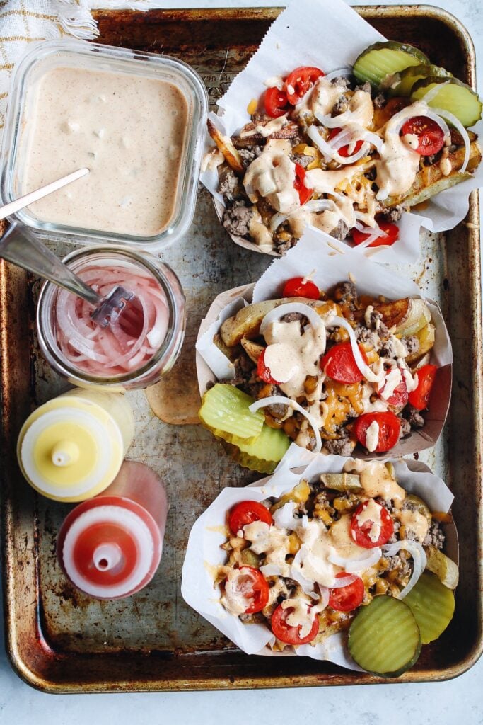 cheeseburger fries in individual serving trays on a baking sheet with condiments