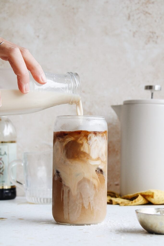 homemade coffee cream being poured into a glass of iced coffee