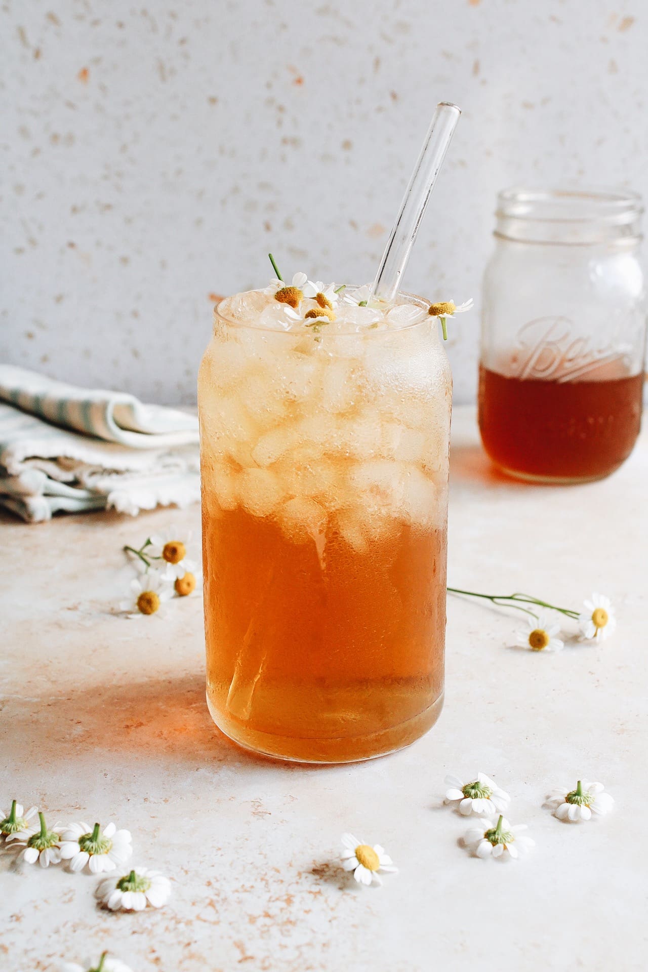 chamomile iced tea in a glass with chamomile flowers scattered around