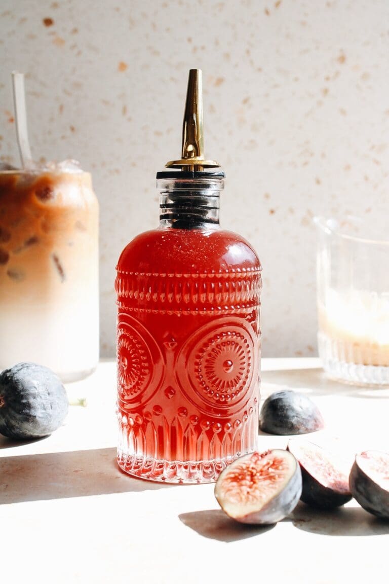fig syrup in a glass bottle with a coffee drink behind it